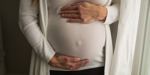 Uma mulher grávida segura a sua barriga perto de uma janela