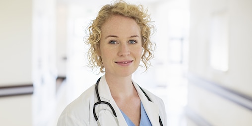 Ξανθιά γυναίκα γιατρός με στηθοσκόπιο χαμογελά σε διάδρομο νοσοκομείου