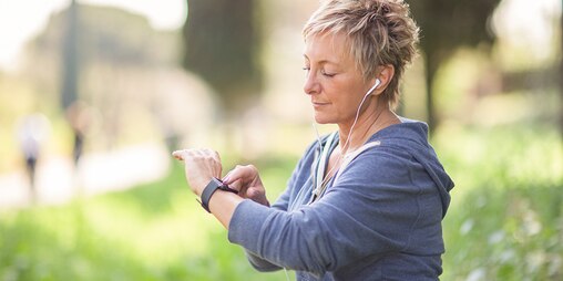 Une joggeuse avec des écouteurs dans les oreilles regarde l’heure sur sa montre