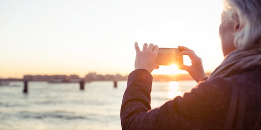 Seniorka fotografuje západ slunce u moře