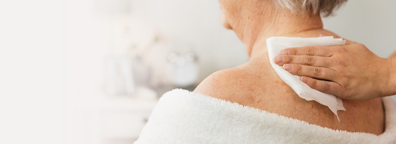 Een plasticvrij vochtig reinigingsdoekje van TENA wordt gebruikt om de huid van een oudere persoon te reinigen.