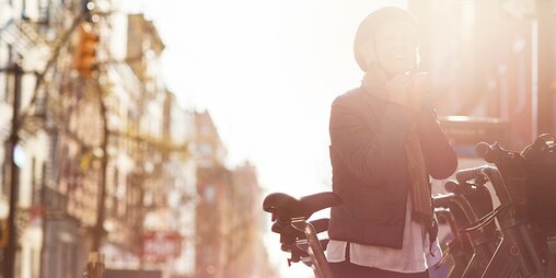 In piedi tra le biciclette, in città, una donna dall’aspetto felice indossa il casco 