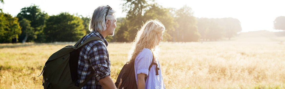 Volwassen man en vrouw met rugzakken op, aan de wandel in een zonnig veld