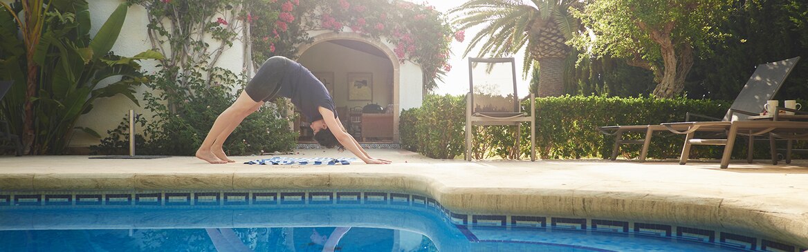 Egy nő jógázik a medencénél egy üdülőház előtt, a szabadban