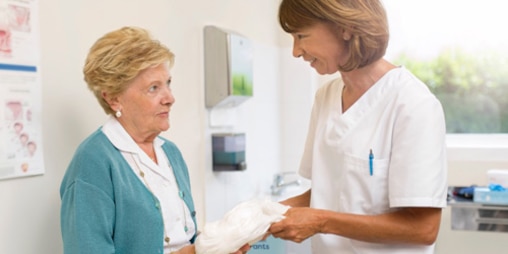 Gydytoja savo kabinete senyvo amžiaus pacientei rodo, kaip naudoti šlapimo nelaikymo priemones.