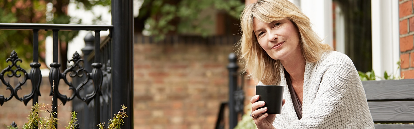 Žena uživa u šolji čaja na svom tremu ispred kuće od cigala Žena uživa u šolji čaja na svom tremu ispred kuće od cigala