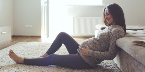 A pregnant woman holds her belly while sitting on the floor
