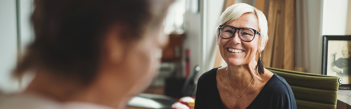 Eine fröhliche ältere Frau mit Laptop spricht mit einer Kollegin im Home Office