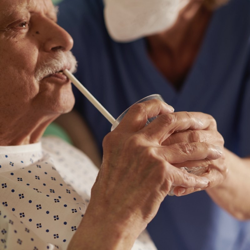 Une infirmière aide un patient atteint de SEP à tenir un verre d'eau.