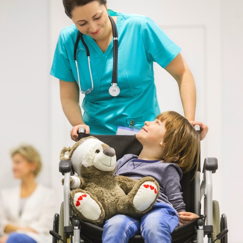 Un jeune garçon lève la tête et sourit à l'infirmière qui le pousse dans son fauteuil roulant.