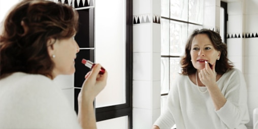 Mujer pintandose los labio en frente de un espejo