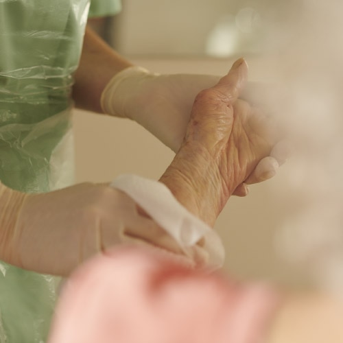 Une infirmière nettoie le bras d'une personne âgée avec une lingette humide.