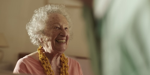 Care home resident laughs together with a nurse while sitting down.