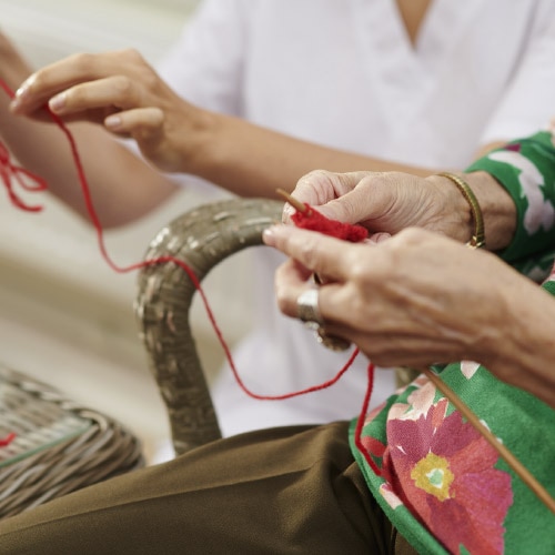 Une personne âgée tricote avec un fil rouge