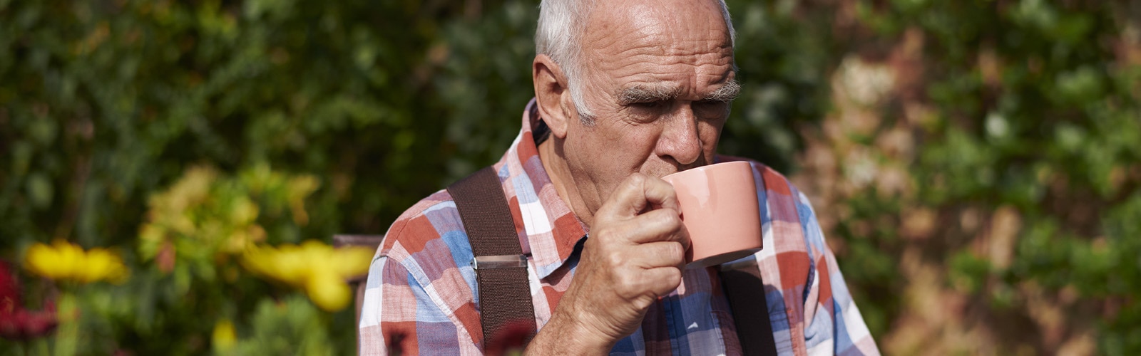 Man sitting in a garden drinking from a mug. 