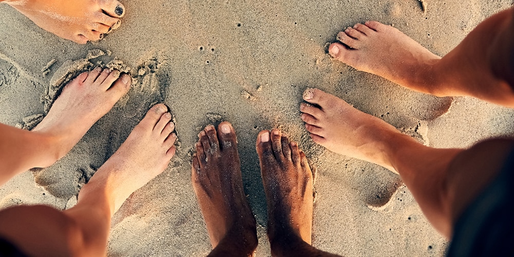 Närbild av fyra par bara fötter i sanden 