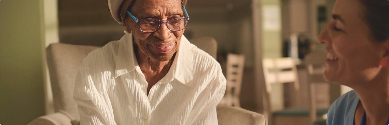 A professional caregiver smiles towards a female nursing home resident.