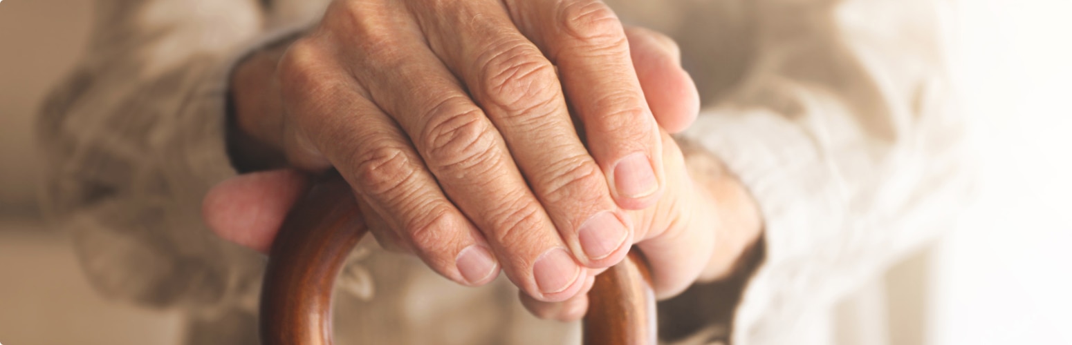 A close-up image of elderly, female hands holding a walking stick