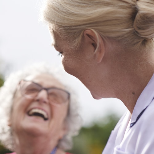 A smiling elderly female resident taking a walk outdoors with a professional caregiver
