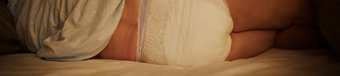 A pair of TENA Intimates Overnight Underwear incontinence Underwear are worn by an older person sleeping soundly in their bed. 