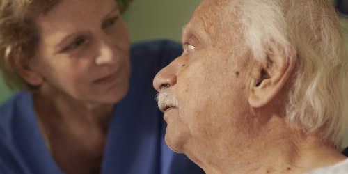 شخص مُسن بشعر أبيض يجلس مرتدياً رداءً أزرق.