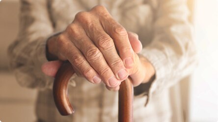 A close-up image of elderly, female hands holding a walking stick.