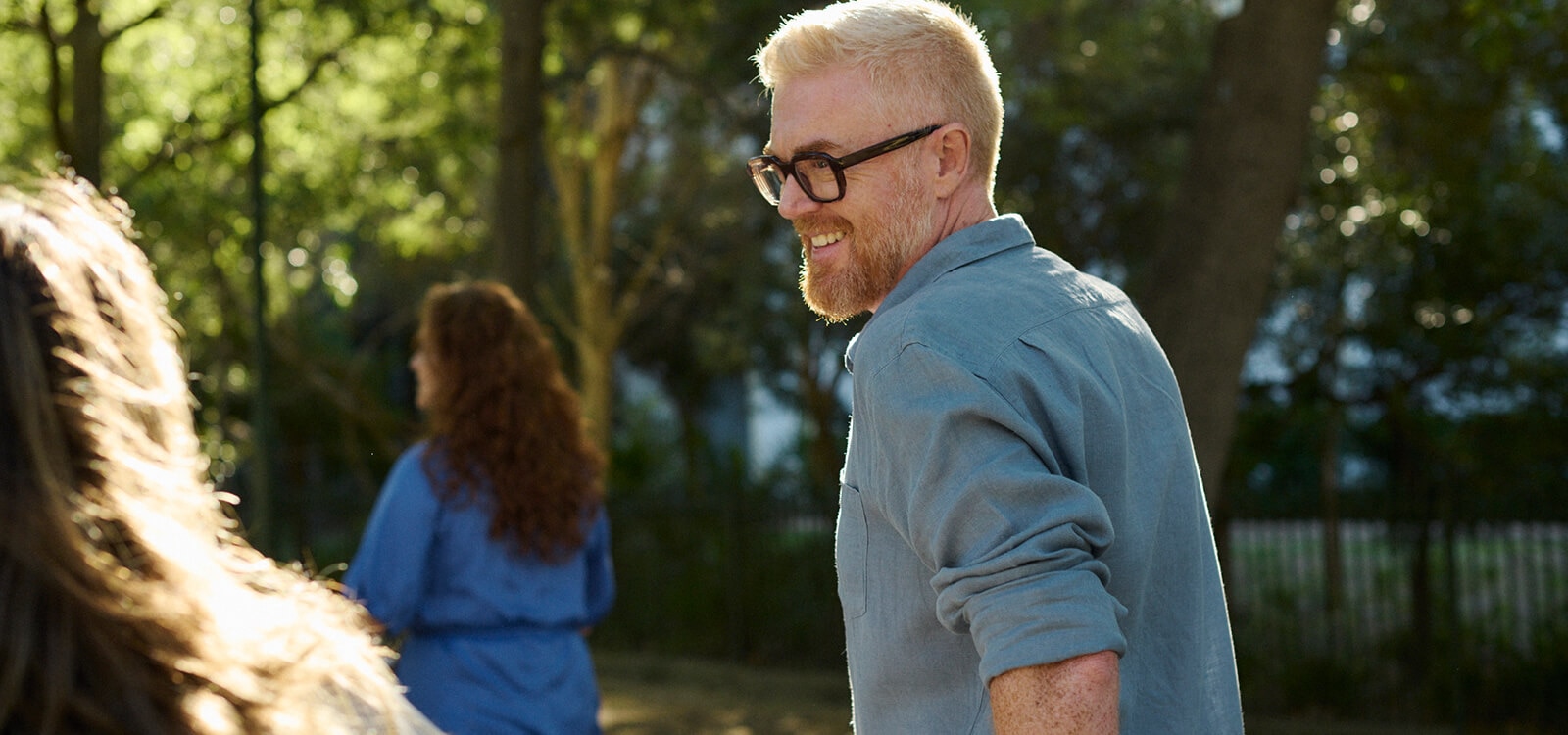 Varias personas paseando en un parque rodeado de árboles, iluminado por la luz del sol.