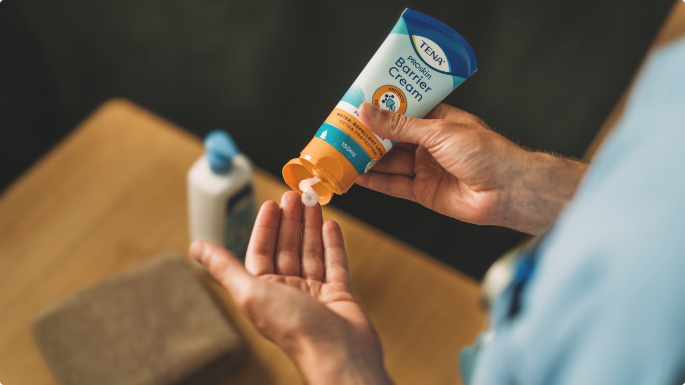 Eine professionelle Pflegekraft drückt die TENA ProSkin Barrier Cream auf ihre Hand, damit sie aufgetragen werden kann.