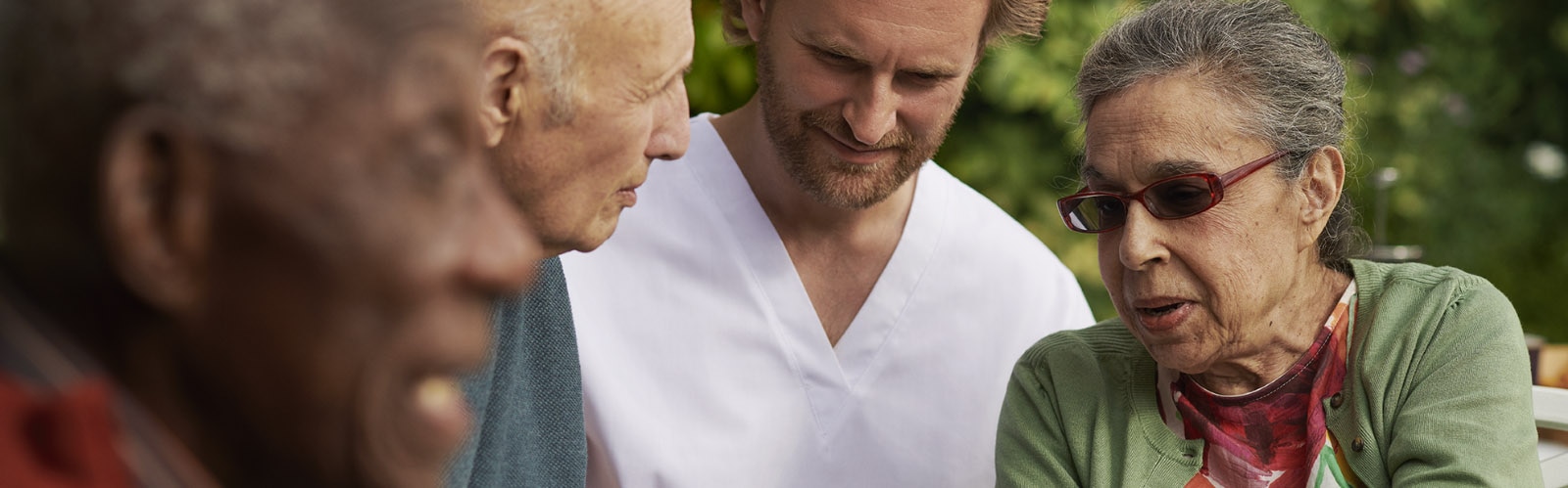 介護施設の入居者たちが外に座り、看護師と一緒に笑い合っている 介護施設の入居者たちが外で看護師と一緒に笑い合っている