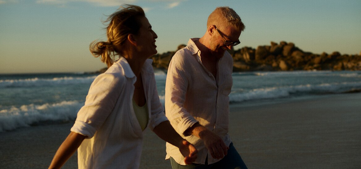 A man and woman hold hands and walk on a beach