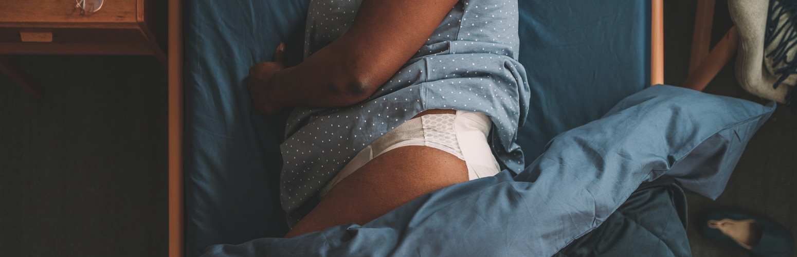 Een professionele zorgverlener houdt een incontinentieverband van TENA ProSkin Flex vast, met op de achtergrond een tevreden cliënt van een zorgorganisatie in bed.