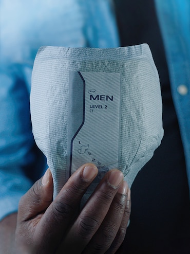 Mužská ruka drží absorpčnú pomôcku TENA určenú pre mužov