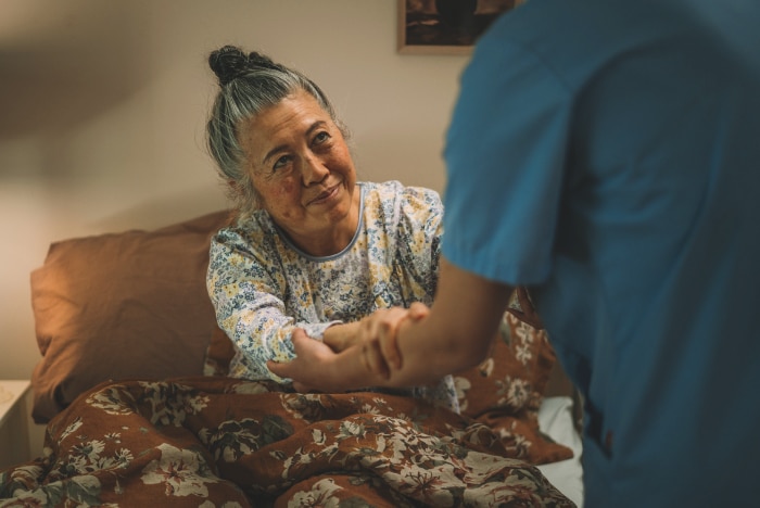 A professional caregiver helps an elderly nursing home resident get up from her bed