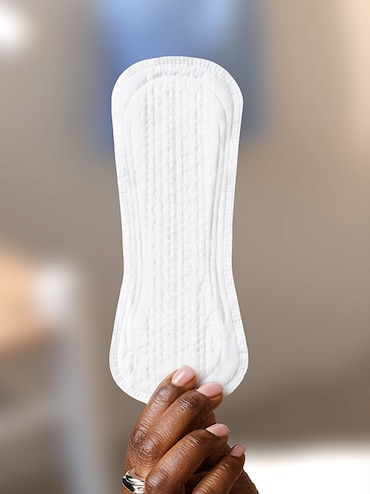 Un TENA Pad per donna tenuto da una mano femminile Un TENA Pad per donna tenuto da una mano femminile