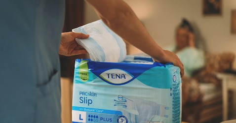 A close-up shot of a professional caregiver’s hands as they remove improved TENA ProSkin Slip from its packaging.