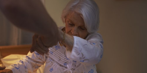 Caregiver is helpding a care home resident out of bed