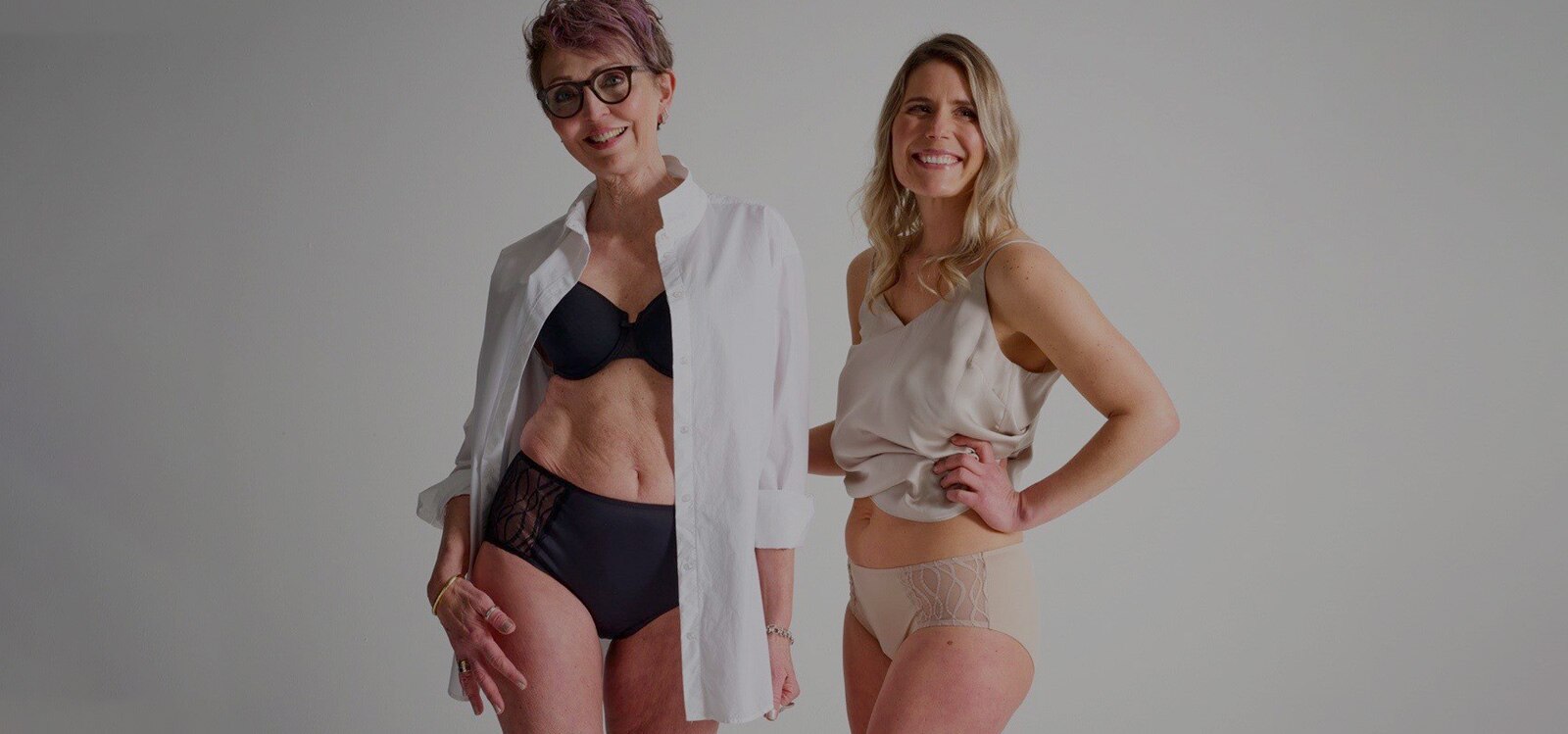 Two women standing next to each other, smiling, wearing TENA Silhouette Washable underwear in black and beige. 