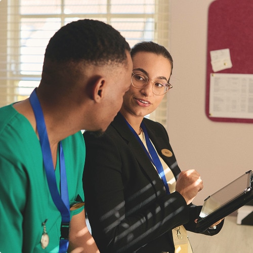 A male professional caregiver talks with a female TENA representative in an office in a nursing home