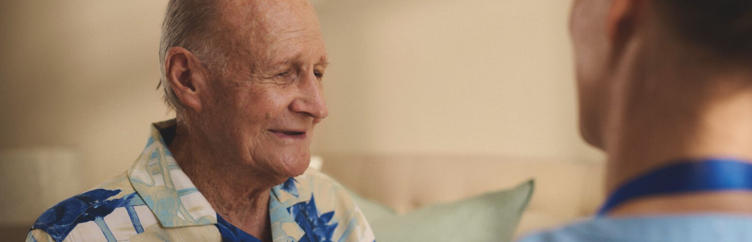 A professional caregiver helps a contented nursing home resident button their shirt