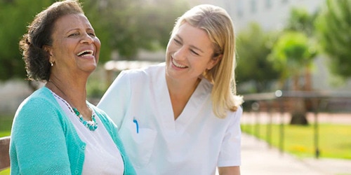 A nurse and care home resident laugh together outdoors.
