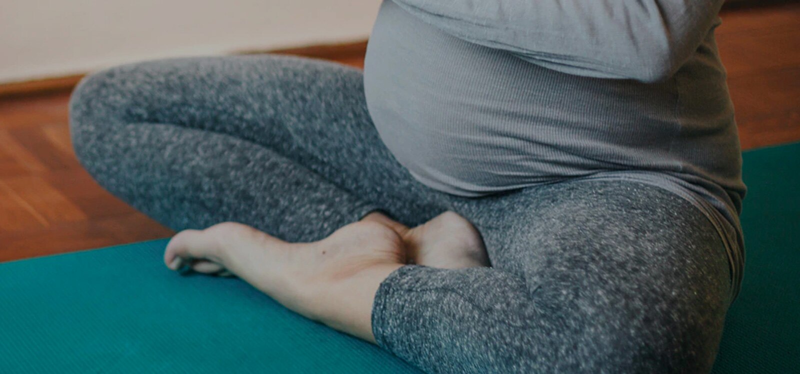 Een zwangere vrouw zit in kleermakerszit op een yogamat
