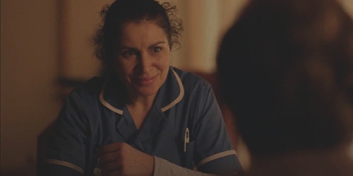 A female professional caregiver sits at a table and smiles at the nursing home resident sitting opposite her. 