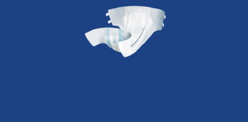 Starszy mężczyzna z siwymi włosami, ubrany w brązową koszulkę polo, siedzi w łóżku i patrzy na kobietę obok niego. W pobliżu stoi pracownik służby zdrowia, częściowo widoczny. Obok łóżka znajduje się stolik nocny z lampką w stylu vintage i szklanką wody, tworząc spokojną i domową atmosferę.