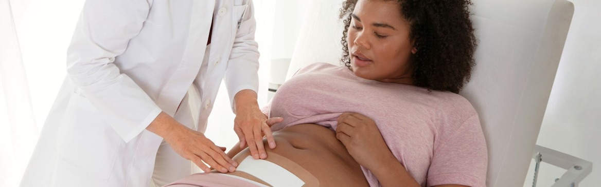 Nurse applying wound dressing to a woman's caesarean wound as she is laid on a hospital bed