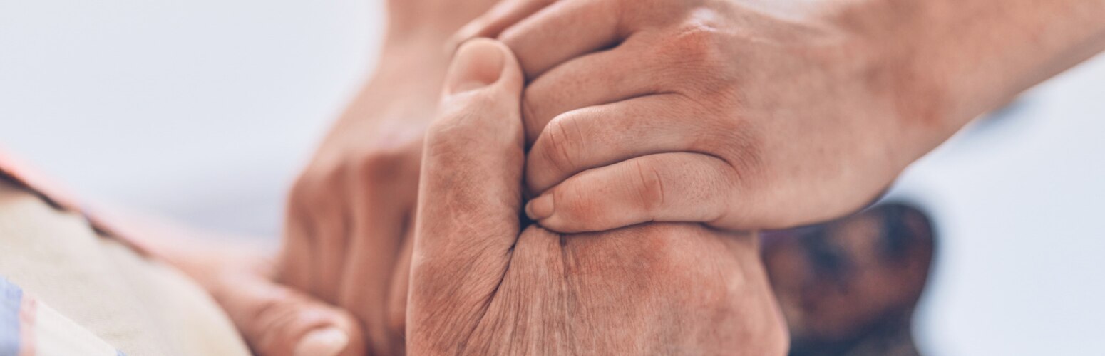 A close-up image of a caregiver’s hand holding the hand of a nursing home resident