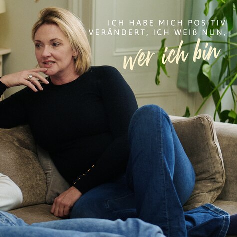 Aby and her female friend are in conversation on the sofa. Text reads: What’s the best thing about the menopause? I’ve changed so much in a positive way, I’m less ambiguous as to who I am.